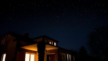 A house with illuminated windows at night under a starry sky, skillfully insulated by a renowned insulation contractor.