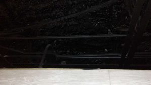Close-up view of a charred attic with burned beams and blackened insulation from a fire, yet the ceiling below remains unscathed. An insulation contractor might be needed to assess and restore the damage.
