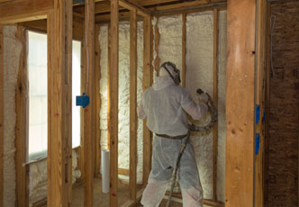 A person in protective gear sprays foam insulation on a wooden framework inside a building under construction, showcasing the expertise of an insulation company Baton Rouge.
