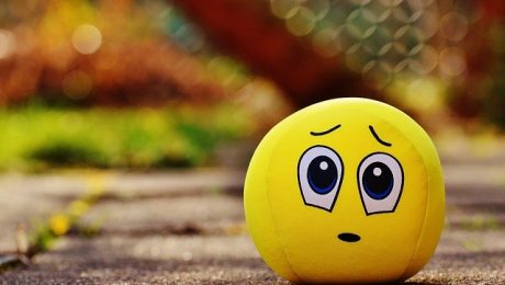 A yellow ball with a worried facial expression sits on a paved surface, seemingly contemplating the work of an insulation contractor, against a blurry, colorful background.
