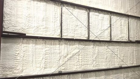 A wall with exposed metal studs and horizontal beams is expertly covered in spray foam insulation by a professional insulation installer.