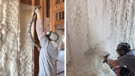 Two contractors from an insulation company in Baton Rouge apply and sculpt polyurethane spray foam insulation on unfinished walls in a building under construction. One person, wearing protective gear, handles the spraying while the other trims the excess foam.
