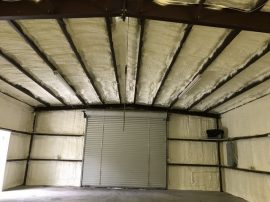 An empty industrial space with insulated walls and ceiling, featuring a large metal roll-up door at the far end, crafted with expertise akin to an insulation installer from New Orleans.