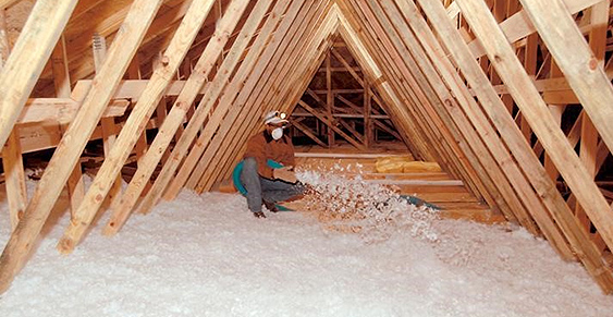 residential-insulation A person wearing a mask and protective gear installs spray foam insulation in the attic of a wooden house framework, expertly handled by an insulation contractor.